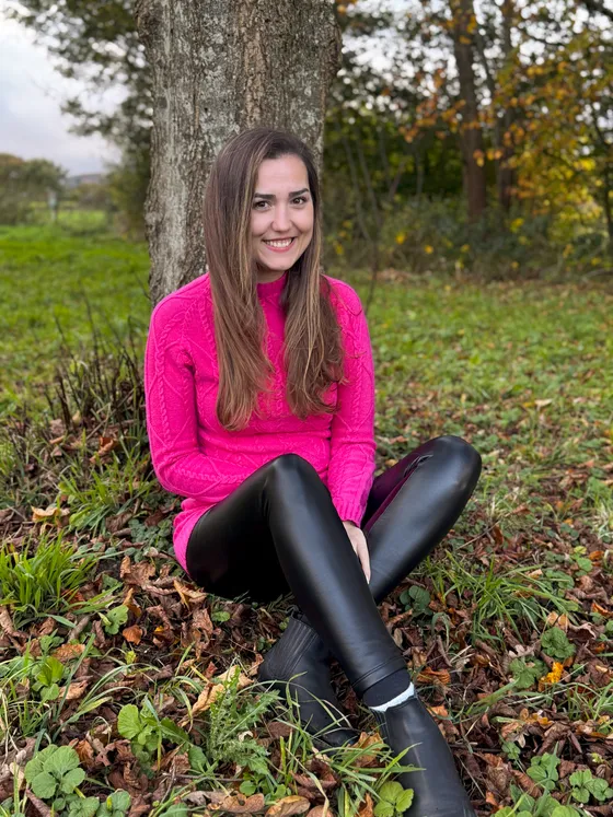 Aleksandra sitzt im Herbst lachend an einen Baum gelehnt
